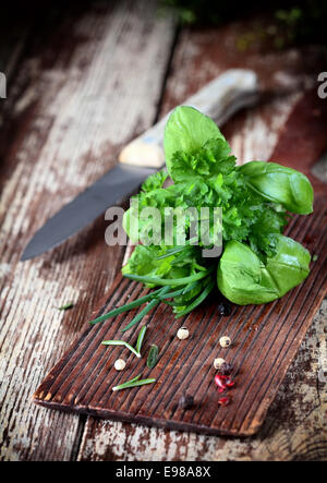 Mazzetto fresco bouquet di erbe garni compresi, rosmarino, prezzemolo, erba cipollina e basilico giacente su un tagliere di legno in una cucina rustica con un coltello Foto Stock