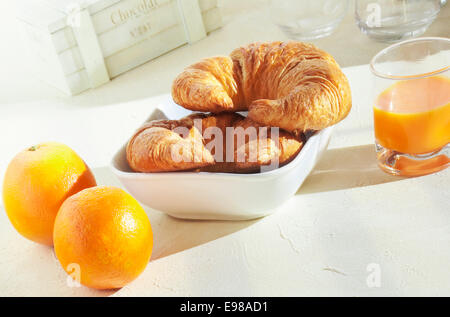 Pasto sano di arance fresche e croccanti golden croissant per colazione la colazione è servita con un bicchiere di spremuta di arancia juic Foto Stock