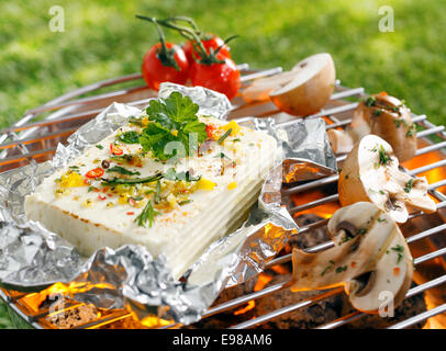 Grande porzione di agguerriti halloumi o il formaggio feta grigliare nel foglio di stagno sui carboni ardenti in un barbecue all'aperto su erba verde Foto Stock