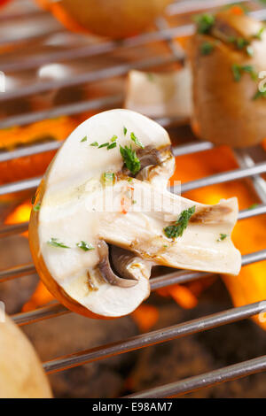 Fresh dimezzato i funghi spolverati con un trito di erbe per aromatizzare la cottura alla griglia su un barbecue fire Foto Stock