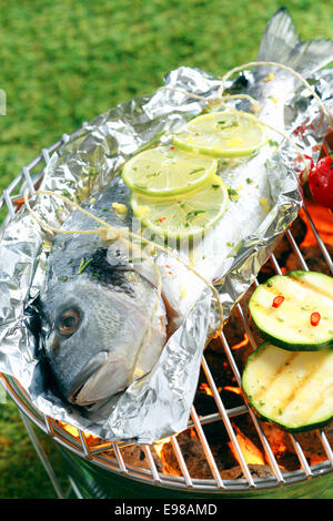 Intero fresco orata breem guarnite con spicchi di limone tostatura su un foglio di alluminio sopra i carboni ardenti in un barbecue Foto Stock