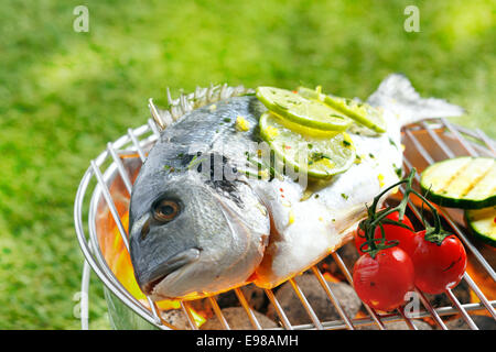 Tutto orata breem guarnite con fettine di limone la tostatura alla brace su un barbecue esterno con maturi pomodori ciliegia sulla Foto Stock