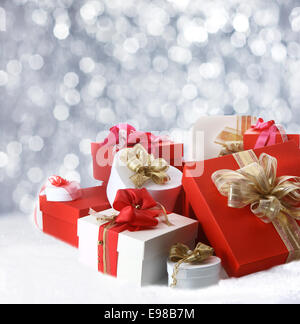 Raccolta di festosa decorazione regali di Natale in rosso, bianco e oro giacente in inverno la neve contro un bokeh di partito spumanti Foto Stock