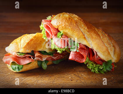 Deliziosi salumi e prosciutto baguette con lattuga fresca e basilico su una vecchia cucina in legno tavolo Foto Stock