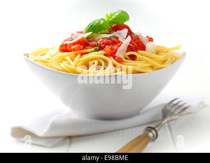 La pasta in una ciotola bianco con salsa di pomodoro e basilico fresco insieme contro un tovagliolo bianco su un tavolo bianco. Foto Stock