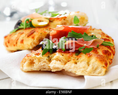 Delizioso pane appena sfornato tradizionale focaccia italiana con prosciutto, olive e rucola su un tovagliolo bianco, vista ravvicinata Foto Stock