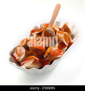 Piccante salsiccia affumicata con ketchup servita tagliata a fette in un decorativo bianco scanalati ciotola con una piccola forcella in legno Foto Stock