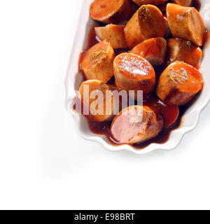 Chiudere fino ad alto angolo di visione delle fette di grigliate di salsiccia affumicata in salsa barbecue in un piccolo piatto scanalati su sfondo bianco con copyspace Foto Stock