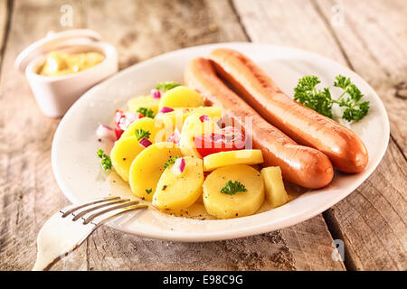 Due grigliate di salsicce viennesi con il bambino di patate, erbe e pomodoro su una piastra bianca su un rustico di una superficie di legno Foto Stock