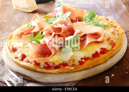 Pizza italiana e rabboccato con prosciutto e fresche foglie di rucola su una base di formaggio e pomodoro servita su un legno rustico Foto Stock