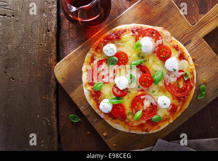 Vista aerea di un colorato gourmet pizza italiana con una varietà di formaggi, pomodoro e basilico fresco su un tagliere di legno Foto Stock