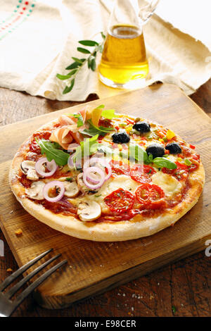 Cucina italiana quattro stagioni pizza con tutti i condimenti tra cui il prosciutto crudo, olive, funghi, formaggi, pomodoro, cipolla, rucola e basilico per un delizioso pasto salato Foto Stock