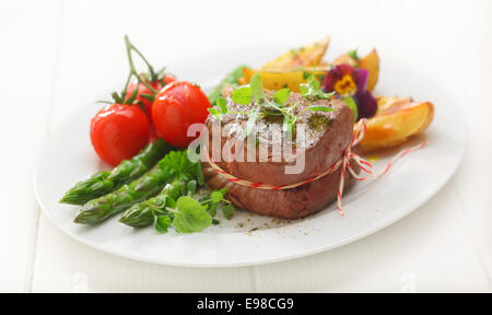 Deliziosa porzione spessa di grigliate di filetto di manzo servita con prodotti freschi Asparagi verdi spears, di patata e di pomodoro Foto Stock