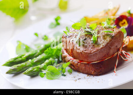 Medaglione di arrosto di filetto di manzo legato con una corda e servita con prodotti freschi di punte di asparagi verdi e lance liberalmente guarnita con Foto Stock