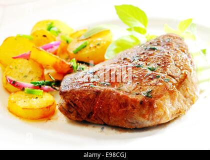 Grande porzione di spessi succosa bistecca con nitide golden patate arrosto, la cipolla e le erbe fresche su una piastra bianca, primo piano Foto Stock