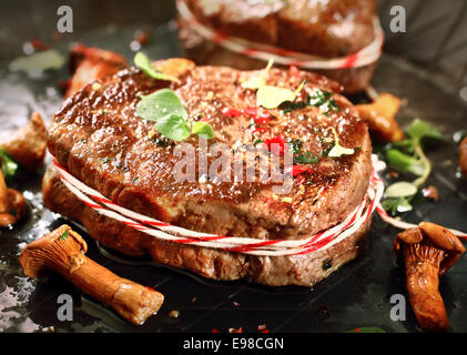 Primo piano di una gustosa grigliata di medaglione di filetto e funghi conditi con spezie e erbe aromatiche fresche Foto Stock