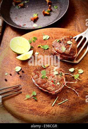 Vista aerea di un tagliere di legno in cucina con utensili per pan arrostire due deliziosi piatti succulenti medaglioni di filetto di manzo Foto Stock