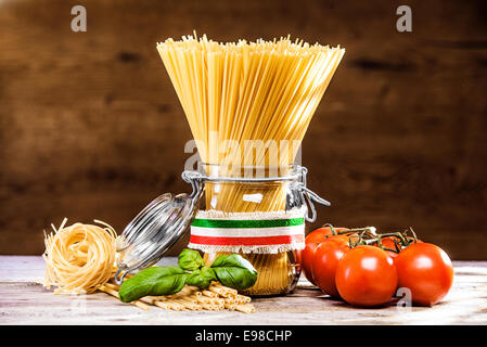 Bundle cruda essiccata spaghetti italiano legate con un nastro con i colori della bandiera nazionale - rosso, bianco e verde - in piedi in un vasetto di vetro con pomodori , fettucini e basilico Foto Stock