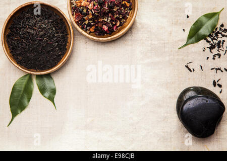 Miscele di fresco essiccato shredded foglie di tè in piccoli recipienti su un tessuto a trama backgorund con Basalto Liscio pietre spa concettuale del supplente naturopatia con copyspace Foto Stock