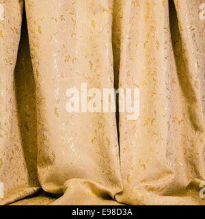 Texture di sfondo di drappeggi di golden damasco con un brillante self patterning di fiori e foglie di acanto appeso nella lussureggiante pieghe morbido per un elegante decor interno Foto Stock