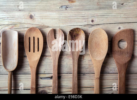 Riga assortiti di vecchia cucina in legno utensili giacenti su un grungy incrinato superficie di legno in una cucina di paese Foto Stock