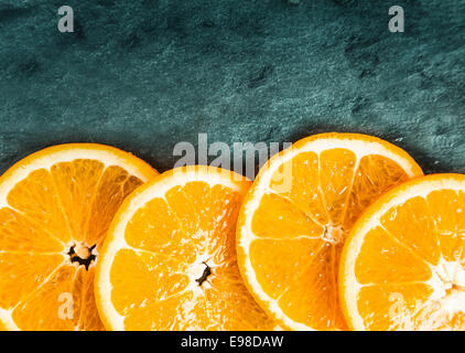 Colorate fresche succose fette di arancio disposte come un confine inferiore su ardesia testurizzata con angolo superiore vignettatura e copyspace Foto Stock