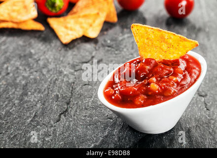 Servire calda in salsa piccante salsa fatta con pomodoro e peperoncino in una ciotola con tortilla di mais o nachos a tuffo per un saporito Foto Stock