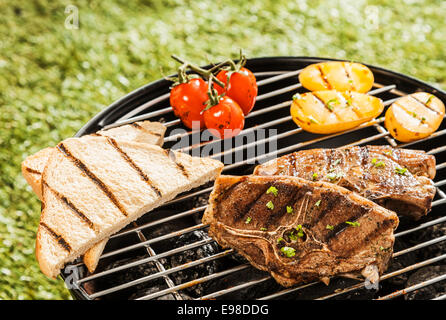 Delizioso pranzo alla griglia su un barbecue con costolette di agnello, pomodori, patate e fette di pane tostato in attesa di essere servito in un giorno di estate Foto Stock