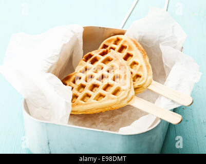 Divertimento crisp golden heart-shaped waffle ghiaccioli con il tradizionale schema a nido d'ape e un bastone di legno su carta sgualcita in un stagno Foto Stock