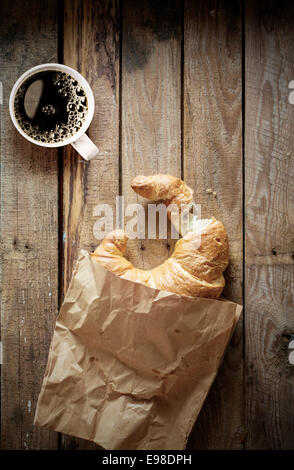 Sfoglia fresca golden croissant con un morso mancante e una tazza di forte colore nero caffè espresso su un vecchio sfondo di legno con copyspace, vista aerea Foto Stock