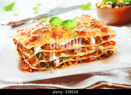 Close-up di un tradizionale lasagne fatte con carne macinata ragù alla bolognese e rabboccato con foglie di basilico servito su una piastra bianca Foto Stock