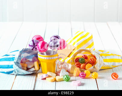 Assortimento di molti tipi di caramelle con marshmallows e lollipop in sacchetti e la coppa di cui sopra un bianco tavolo in legno Foto Stock
