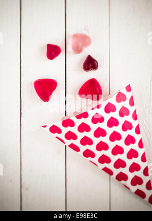 Vista dall'alto di un cono di caramella decorata con cuori rosa fuoriuscita a forma di cuore ad caramelle gommose oltre un legno bianco bordo tabella Foto Stock