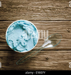 Close up vista aerea di una vasca del blu gourmet gelato italiano con un cucchiaio di plastica servita su un vecchio tavolo di legno, in piazza Foto Stock