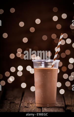 Frullato al cioccolato o frullato con un frizzante bokeh di luci di partito in background in piedi su una tavola in legno rustico in un
