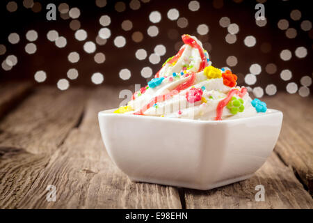 Bambini colorati gelato dessert di partito con un mulinare di ricca crema gelato alla vaniglia e rabboccato con vibrante candy e spruzza decorate con uno sciroppo arancione con un bokeh di scintillanti luci festive Foto Stock