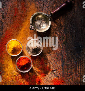 Vista aerea di tre bocce di spice in una cucina di paese su un vecchio ha segnato una superficie di legno con sparsi in polvere e una vecchia succhieruola retrò o setaccio Foto Stock