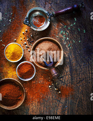 Vista aerea di coloratissimi essiccato le spezie in ciotole spargimento su un vecchio di età ha segnato una superficie di legno in un paese cucina con un setaccio vintage o succhieruola Foto Stock