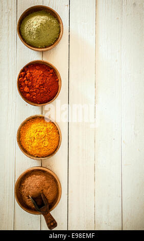 Confine di spezie colorate disposte in una fila verticale con peperoncino, curry, pepe rosso e matcha in polvere in piccole ciotole su uno sfondo del dipinto di bianco per le schede con copyspace Foto Stock