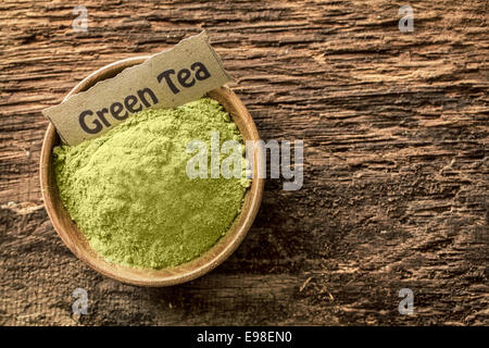 Vista aerea di una piccola ciotola di terra il tè verde in polvere con un nome etichetta utilizzata come una bevanda e un agente aromatizzante in cottura su legno a trama con copyspace Foto Stock