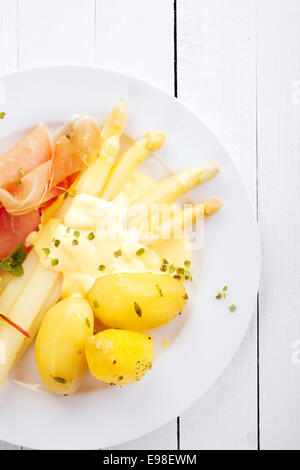 Pasto saporito di asparagi e tagliate a fettine sottili di prosciutto baby con patate bollite e salsa di mayo visto dal di sopra su una piastra bianca sul dipinto di bianco di tavole di legno , closeup Foto Stock