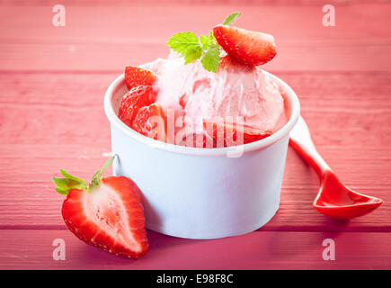 Cool rinfrescante gelato alla fragola o yogurt surgelato dessert servito con fette di fresche fragole mature in una vasca di plastica Foto Stock