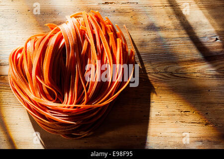 Pomodoro italiano aromatizzato tagliatelli o linguine in piedi pronto per essere aggiunto a un gustoso piatto di pasta su una vecchia cucina in legno contatore nella luce solare pezzata Foto Stock