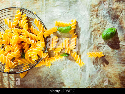 La preparazione di un Italiano fusilli piatto con foglie di basilico fresco e la spirale tradizionali cavatappi pasta sagomata giacente in un vecchio retrò filtro di filo su grunge carta sgualcita all'aperto sotto il sole Foto Stock