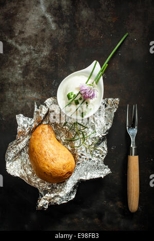 Camicia al forno patata cucinata su un barbecue estivo in un foglio di alluminio è servito fresco con erba cipollina tritata e la panna acida per un delizioso antipasto, vista aerea Foto Stock