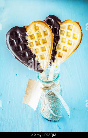 Due romantici a forma di cuore cialde dorato immersi nel cioccolato simbolica dell amore su un bastone in un vasetto di vetro con tag regalo per una fidanzata su un occasione speciale o di celebrazione Foto Stock