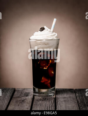 Bicchiere di caffè ghiacciato galleggiante sormontato da un vortice di cremoso gelato alla vaniglia e un solo chicco di caffè in piedi su un rustico in legno vecchio contatore in una caffetteria o coffee house Foto Stock