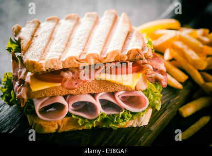 Tostato o grigliate di prosciutto e formaggio club sandwich freschi con lattuga e pomodoro e un lato che serve di patatine, vista ravvicinata Foto Stock