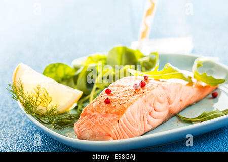 Deliziosa porzione di succulente di grigliati o cotti al forno di filetto di salmone fresco servito con una foglia verde insalata e una fettina di limone per Foto Stock