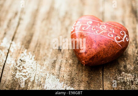 Rosso a forma di pietra come un cuore con intagli su una superficie di legno. Foto Stock